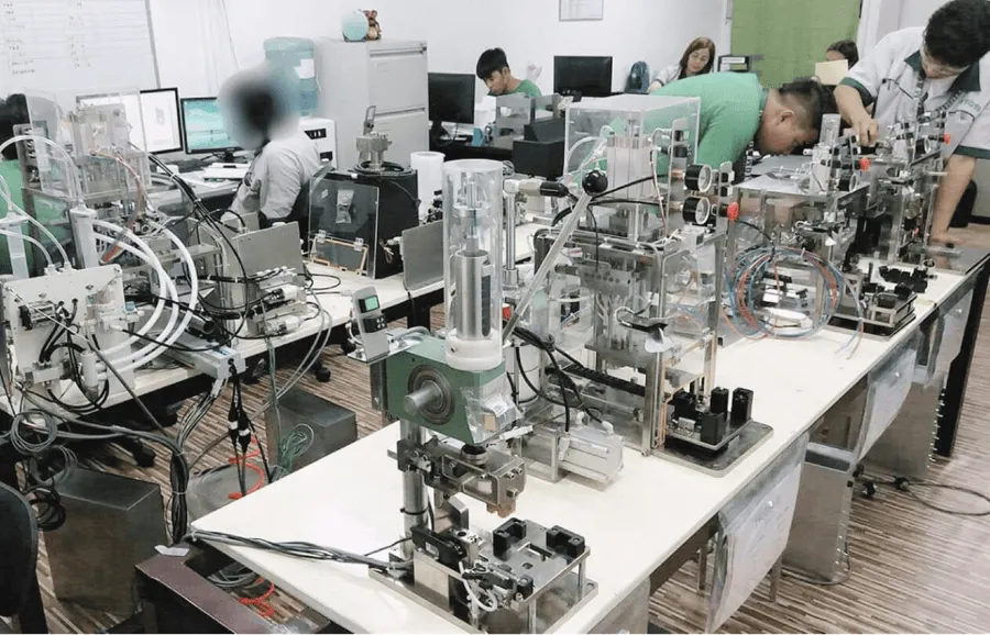 ATOM engineers assembling PLC-controlled automation equipment on the workshop floor, with control panels and pneumatic actuators in view